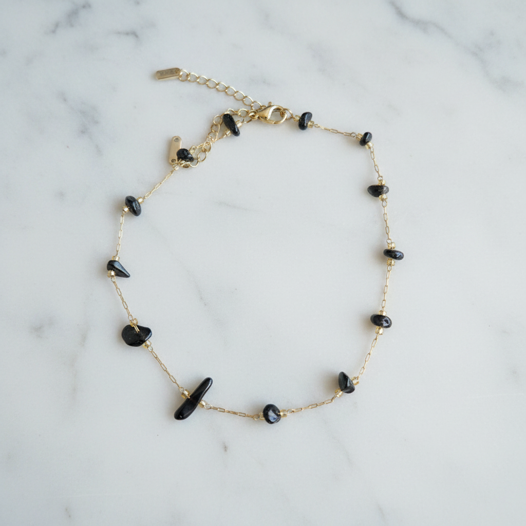Bracelet doré perles noires sur marbre blanc